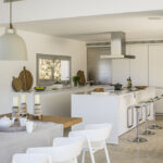 Cocina blanca abierta con isla, campana de acero, taburetes cromados y tablas de cortar de madera