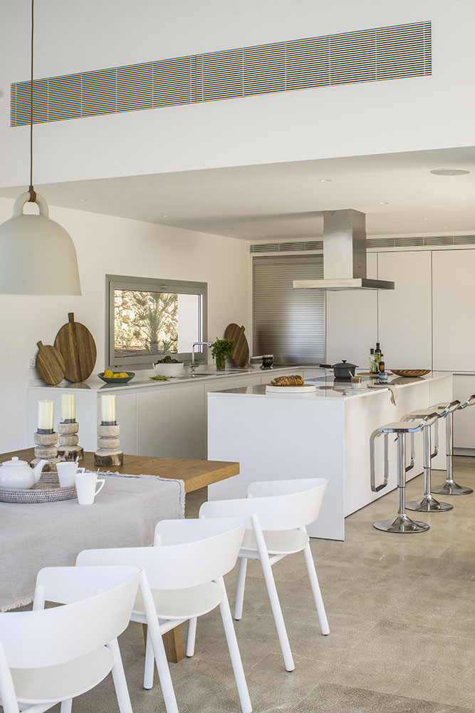 Cocina blanca abierta con isla, campana de acero, taburetes cromados y tablas de cortar de madera