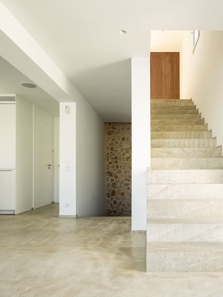 Escalera de piedra clara, muro de mampostería, puerta de madera al fondo y suelo pulido