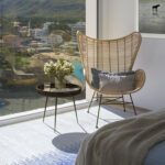 Rincón del dormitorio con butaca de ratán, flores y vistas a la montaña y a la playa