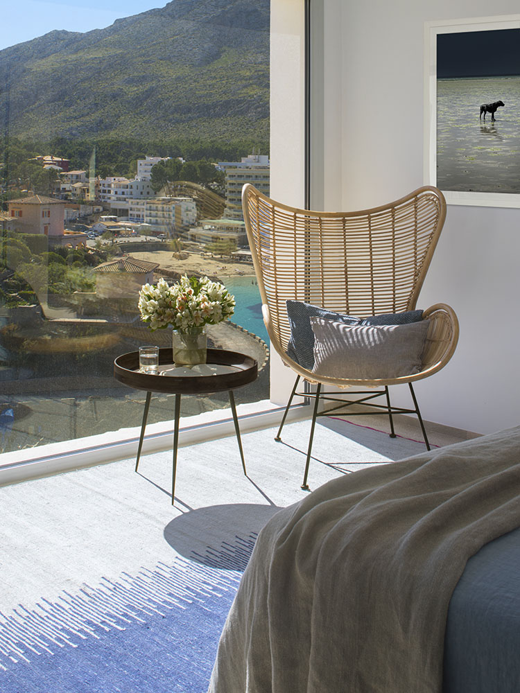 Rincón del dormitorio con butaca de ratán, flores y vistas a la montaña y a la playa