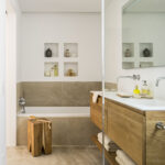 Baño con bañera empotrada, hornacinas blancas, taburete de madera maciza y lavabo sobre mueble de roble