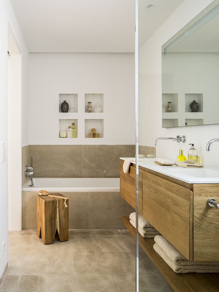 Baño con bañera empotrada, hornacinas blancas, taburete de madera maciza y lavabo sobre mueble de roble
