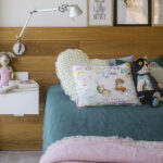 Cama infantil con cabecero de madera, ropa de cama verde, colcha rosa, cojines estampados y lámpara articulada