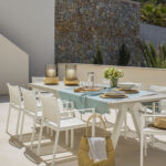 Terraza con mesa de exterior y sillas blancas, mantel turquesa y muro de piedra al fondo