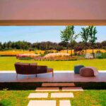 Chaise longue en la terraza con vistas a un prado florido, árboles y camino de losas sobre césped