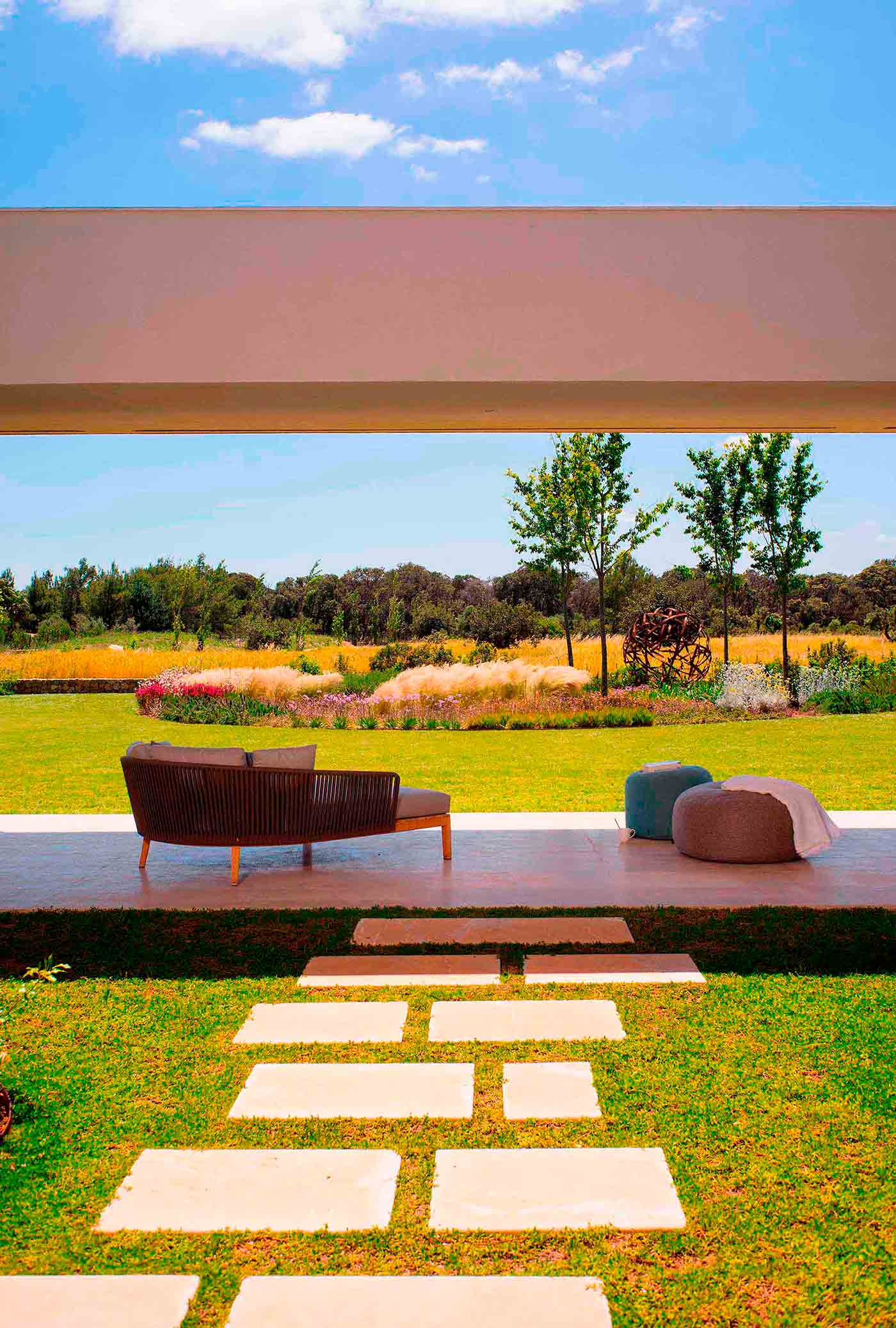 Chaise longue en la terraza con vistas a un prado florido, árboles y camino de losas sobre césped