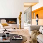 Salón con chimenea empotrada, sillón crema, escultura dorada y paredes de madera al fondo con puerta acristalada