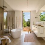 Baño completo con bañera exenta, doble lavabo suspendido, ducha acristalada y ventana alta al jardín