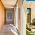 Pasillo con pared de madera, suelo de piedra clara y ventanal a un patio con muro de piedra