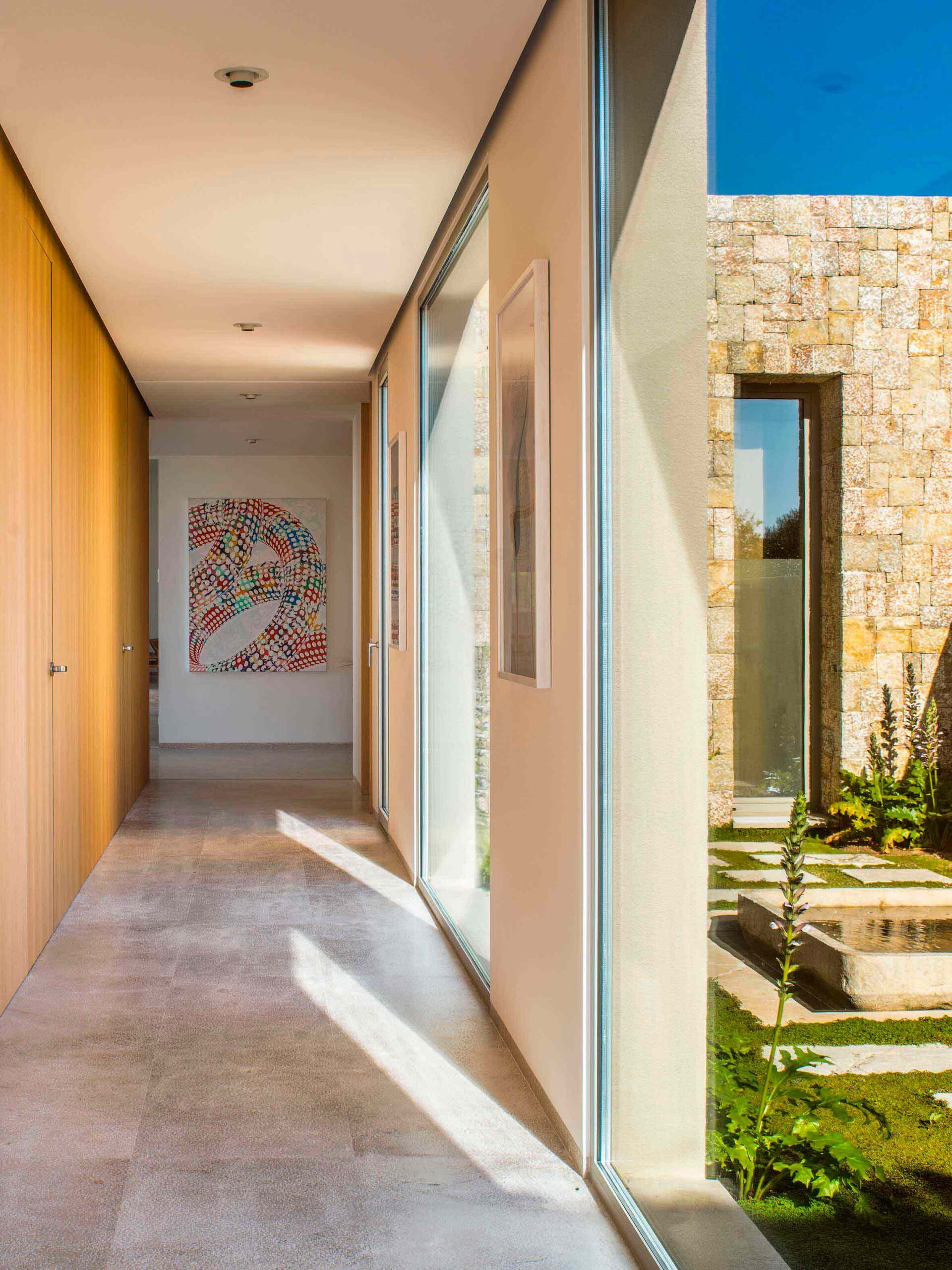 Pasillo con pared de madera, suelo de piedra clara y ventanal a un patio con muro de piedra