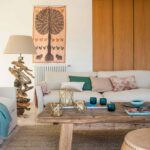 Rincón del salón con tapiz, lámpara de madera flotada, sofá claro y mesa baja de madera rústica.