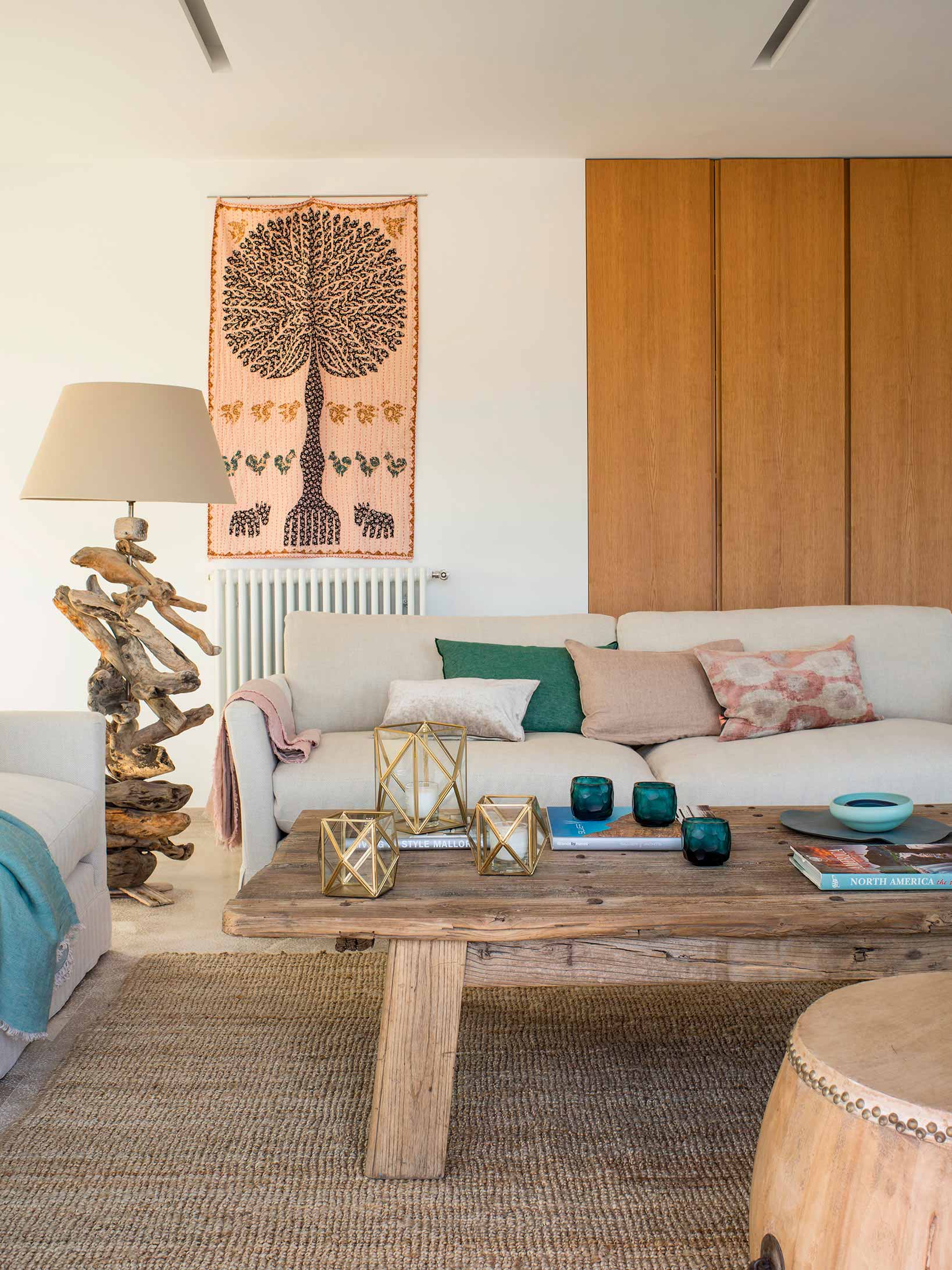Rincón del salón con tapiz, lámpara de madera flotada, sofá claro y mesa baja de madera rústica.