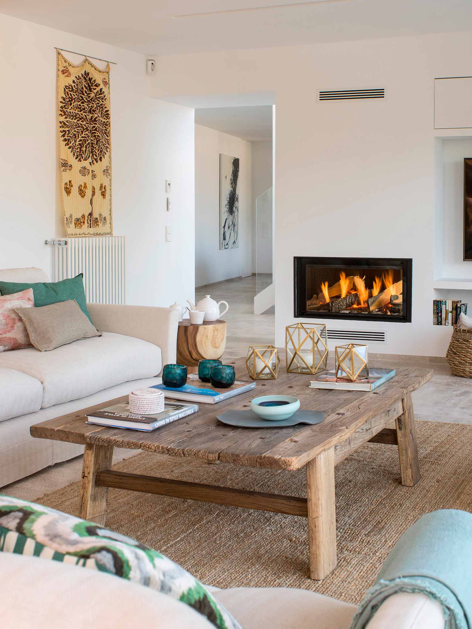 Mesa baja de madera rústica y sofá claro frente a la chimenea, con pasillo al fondo.