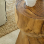 Detalle de mesa auxiliar de madera maciza con taza y tetera blancas, con alfombra de fibra al fondo.