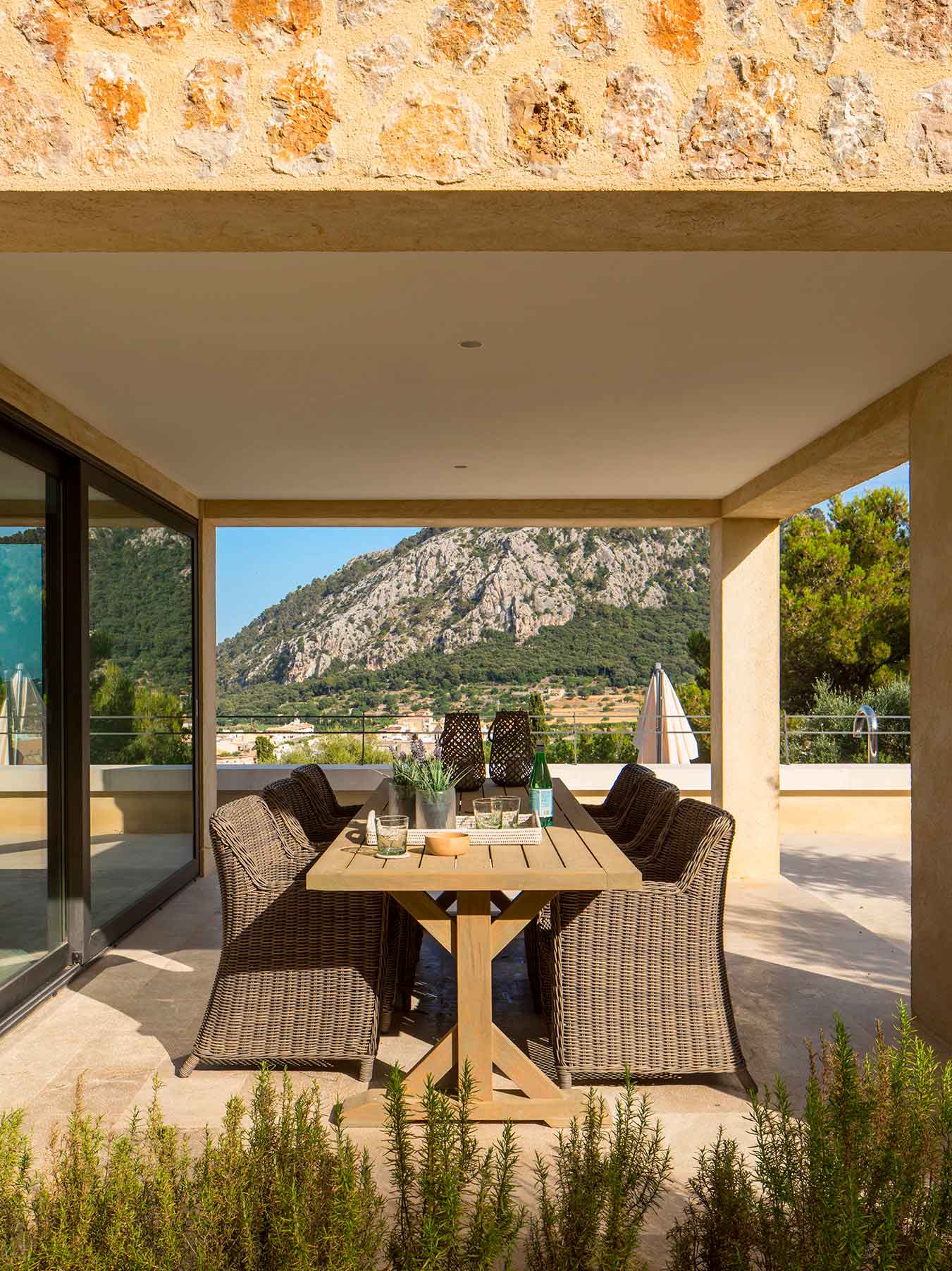 Comedor exterior porticado con sillas de mimbre, mesa de madera y vistas a la montaña.