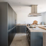 Cocina con columna de armarios gris oscuro, isla con encimera de piedra y campana de acero inoxidable.