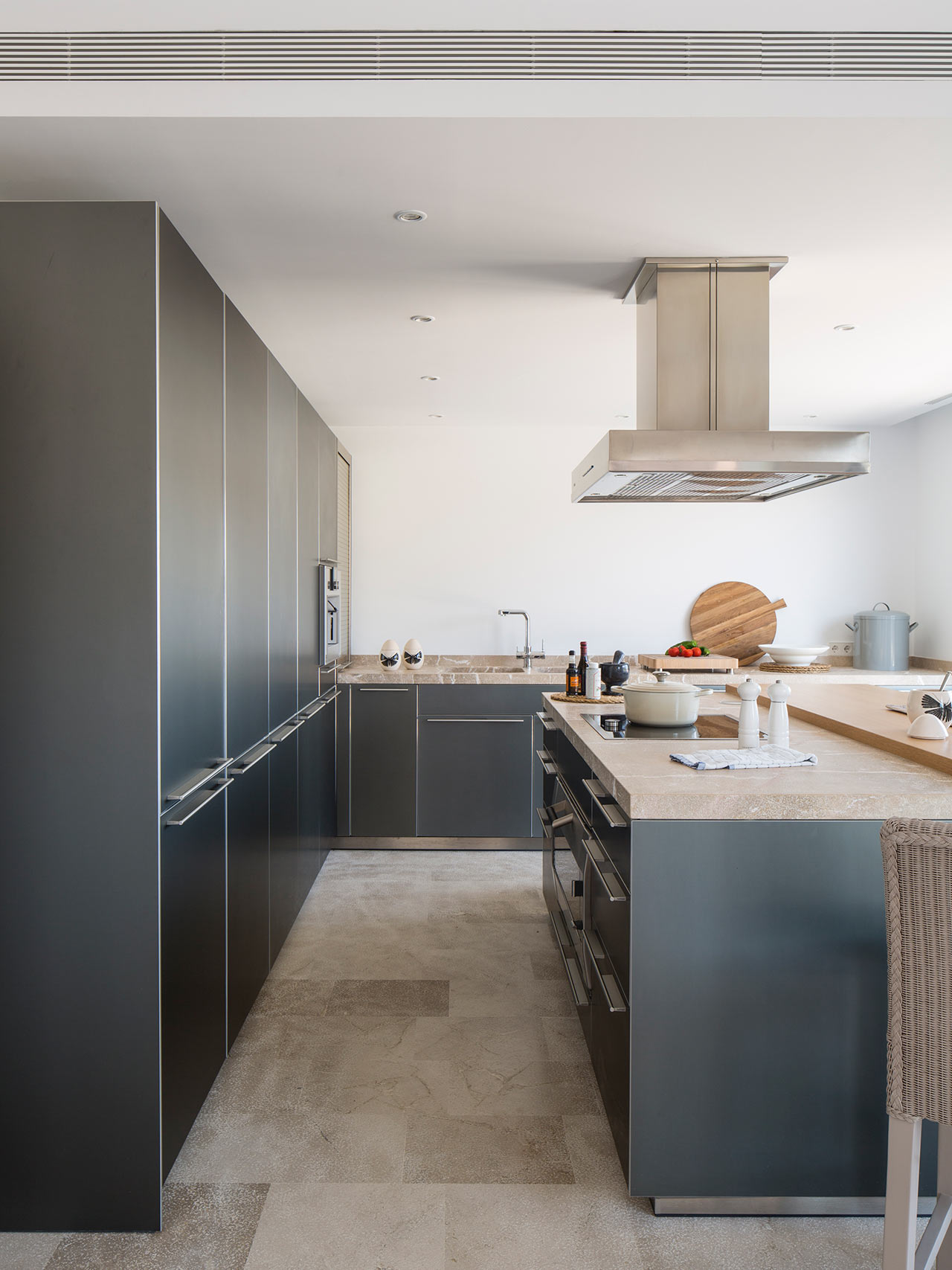 Cocina con columna de armarios gris oscuro, isla con encimera de piedra y campana de acero inoxidable.
