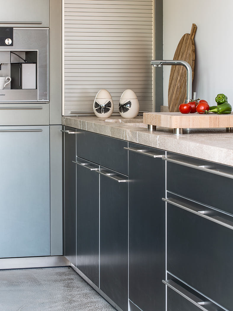 Detalle de puertas de cocina con tiradores metálicos, encimera de piedra y tomates sobre tabla de madera.