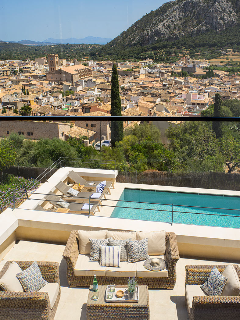 Terraza de estar con sofás de mimbre, piscina con tumbonas y panorama de tejados y montaña.