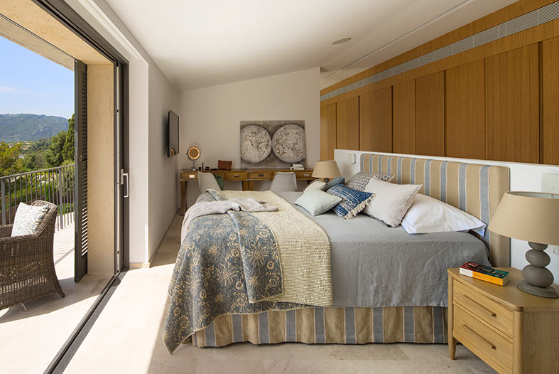 Dormitorio con colcha estampada azul, escritorio de madera, armarios empotrados y balcón con vistas.