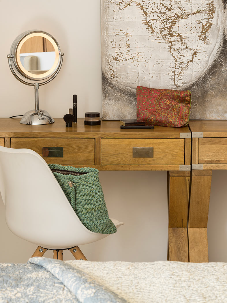 Detalle del escritorio de madera con espejo redondo, silla blanca, bolso verde y cuadro de mapamundi.