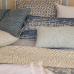 Detalle de cojines estampados en azul y beige, mantas y cabecero de rayas en la cama.