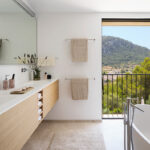 Mueble de lavabo de madera clara, toallas y ventanal con balcón y vistas a la montaña.