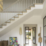Escalera con barandilla de forja blanca con arcos, peldaños de piedra y puerta de cristal al fondo
