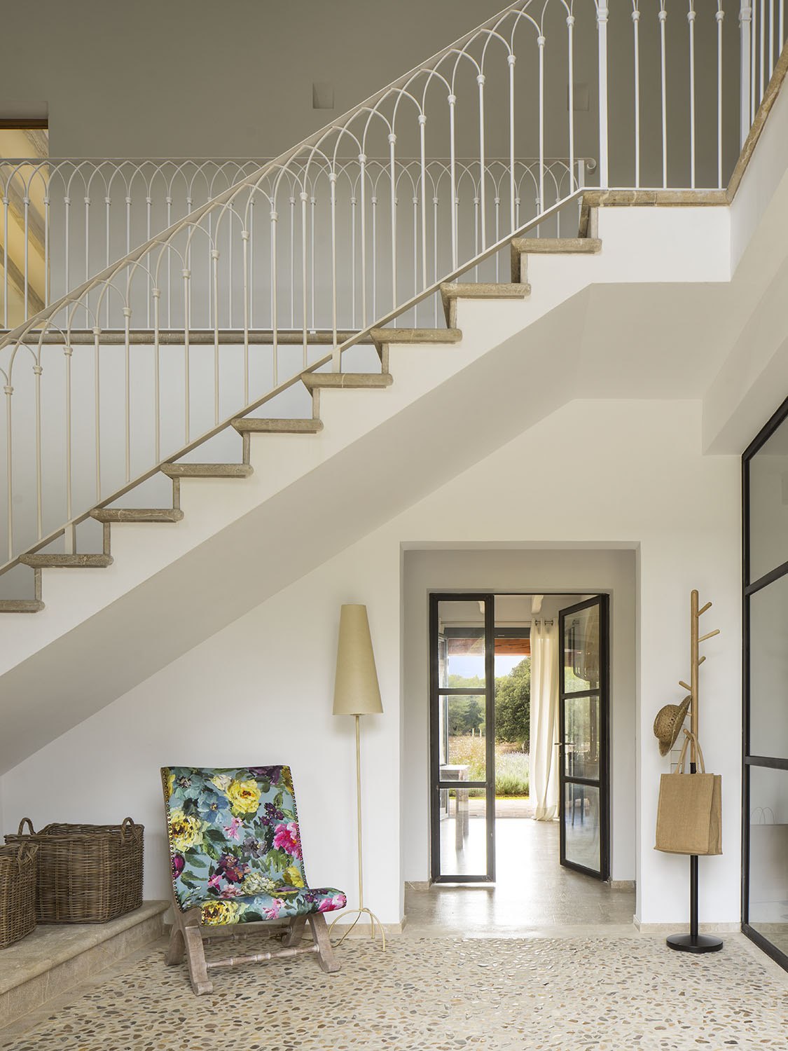 Escalera con barandilla de forja blanca con arcos, peldaños de piedra y puerta de cristal al fondo