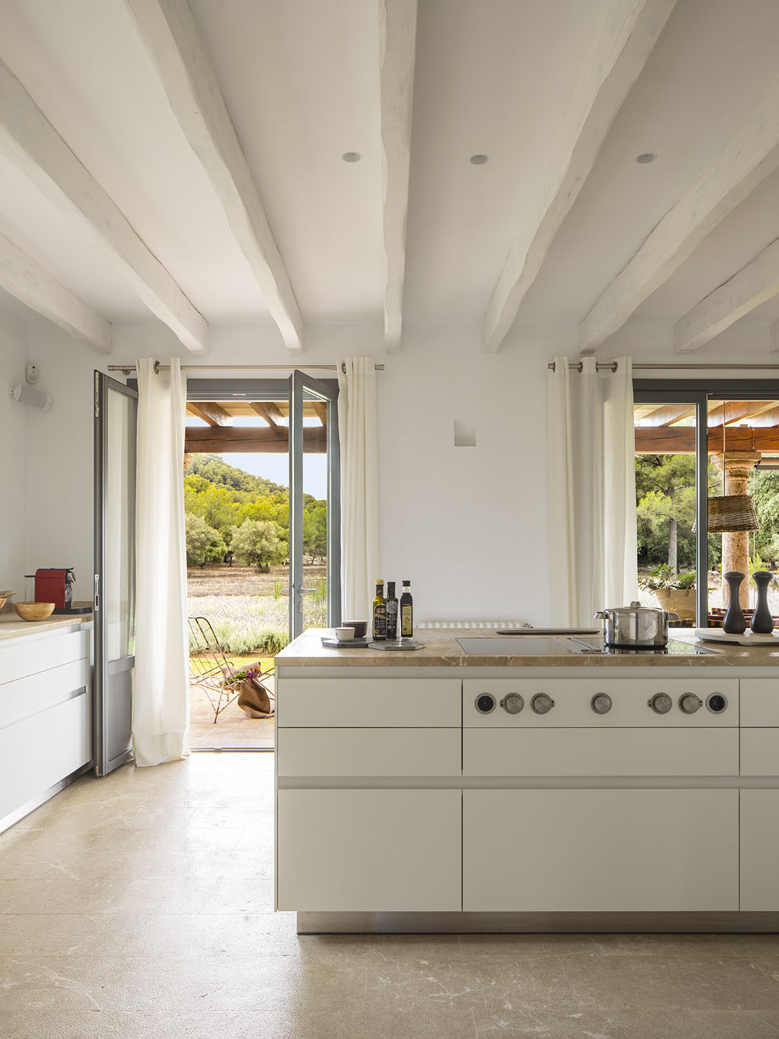Isla de cocina blanca con placa de cocción, vigas blancas y puertas abiertas al porche