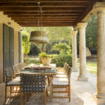 Porche con vigas de madera, columnas de piedra, mesa de comedor exterior y suelo de barro cocido