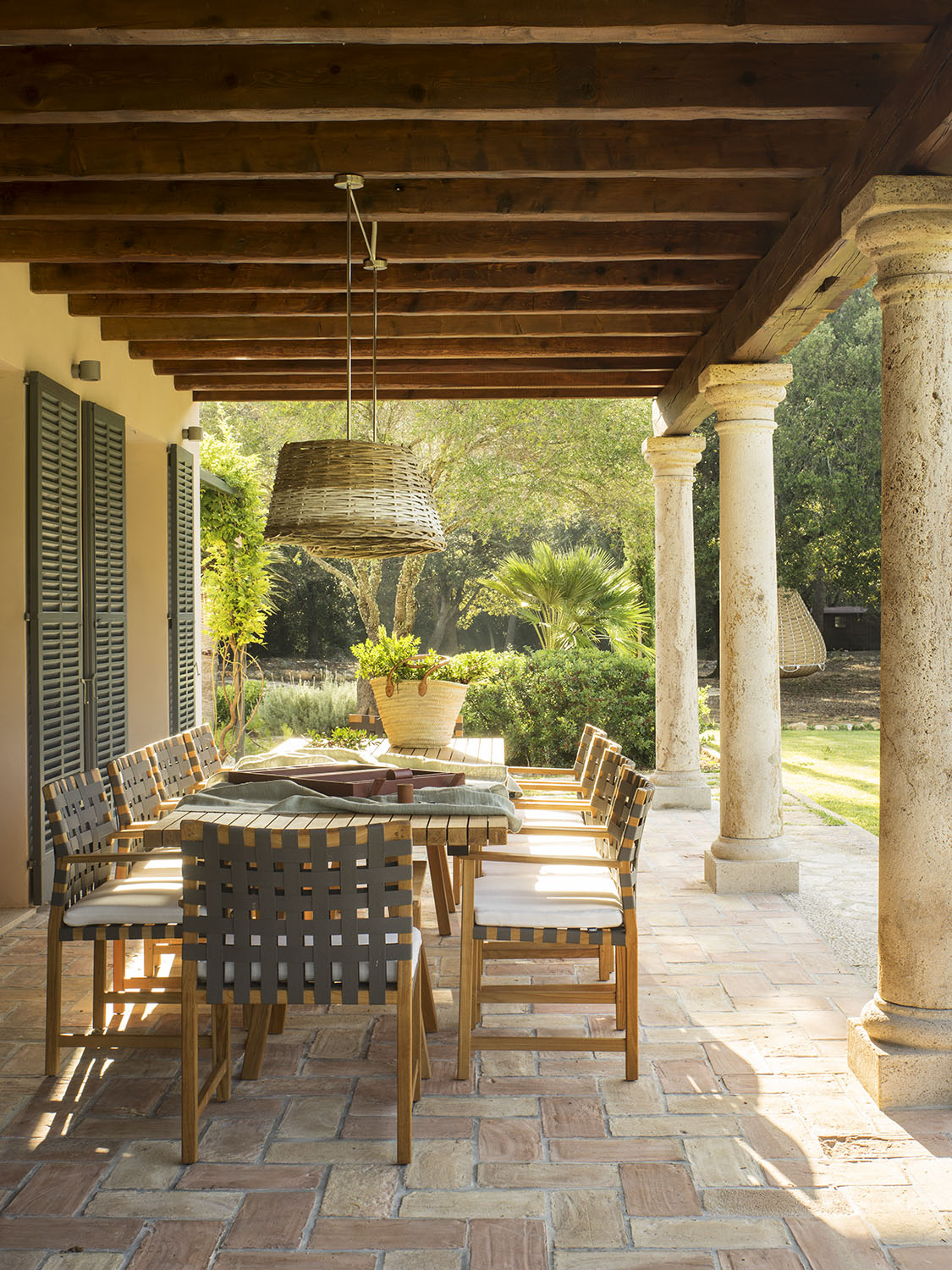 Porche con vigas de madera, columnas de piedra, mesa de comedor exterior y suelo de barro cocido