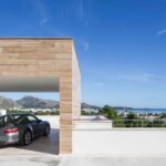 Garaje abierto revestido de madera clara con coche gris y vistas al mar y a las montañas