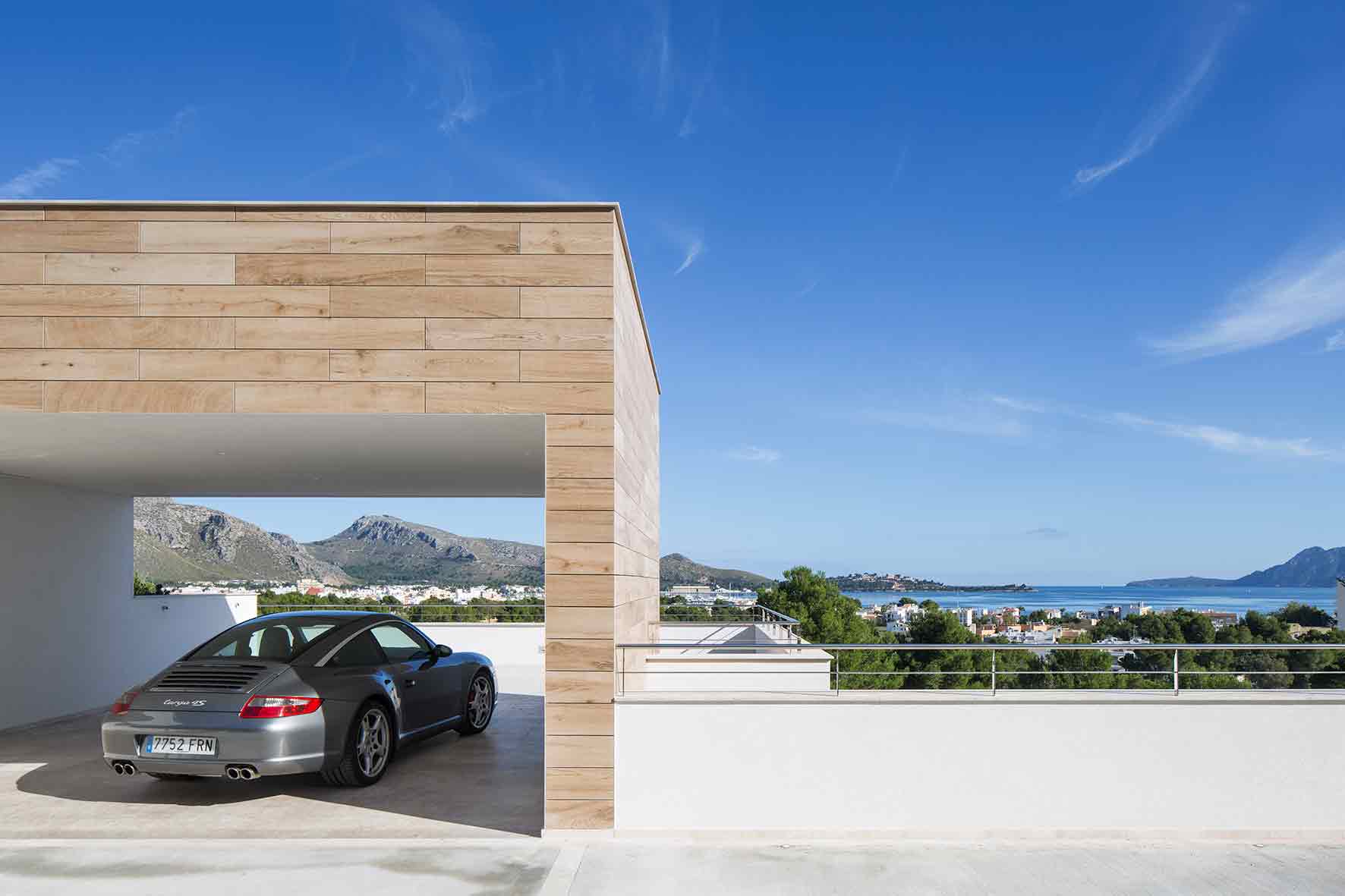 Garaje abierto revestido de madera clara con coche gris y vistas al mar y a las montañas