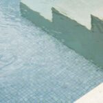Detalle de los escalones de piedra clara y el mosaico azulado del fondo de la piscina