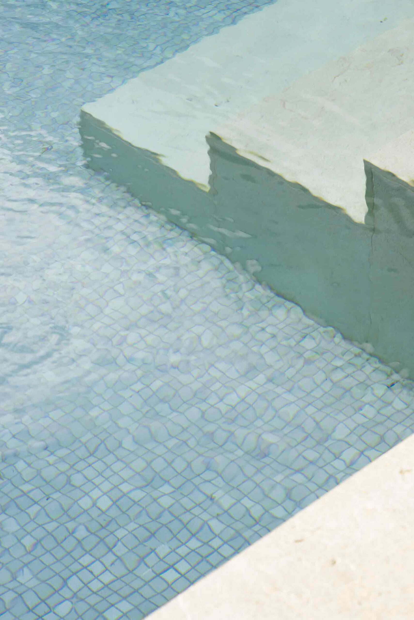Detalle de los escalones de piedra clara y el mosaico azulado del fondo de la piscina