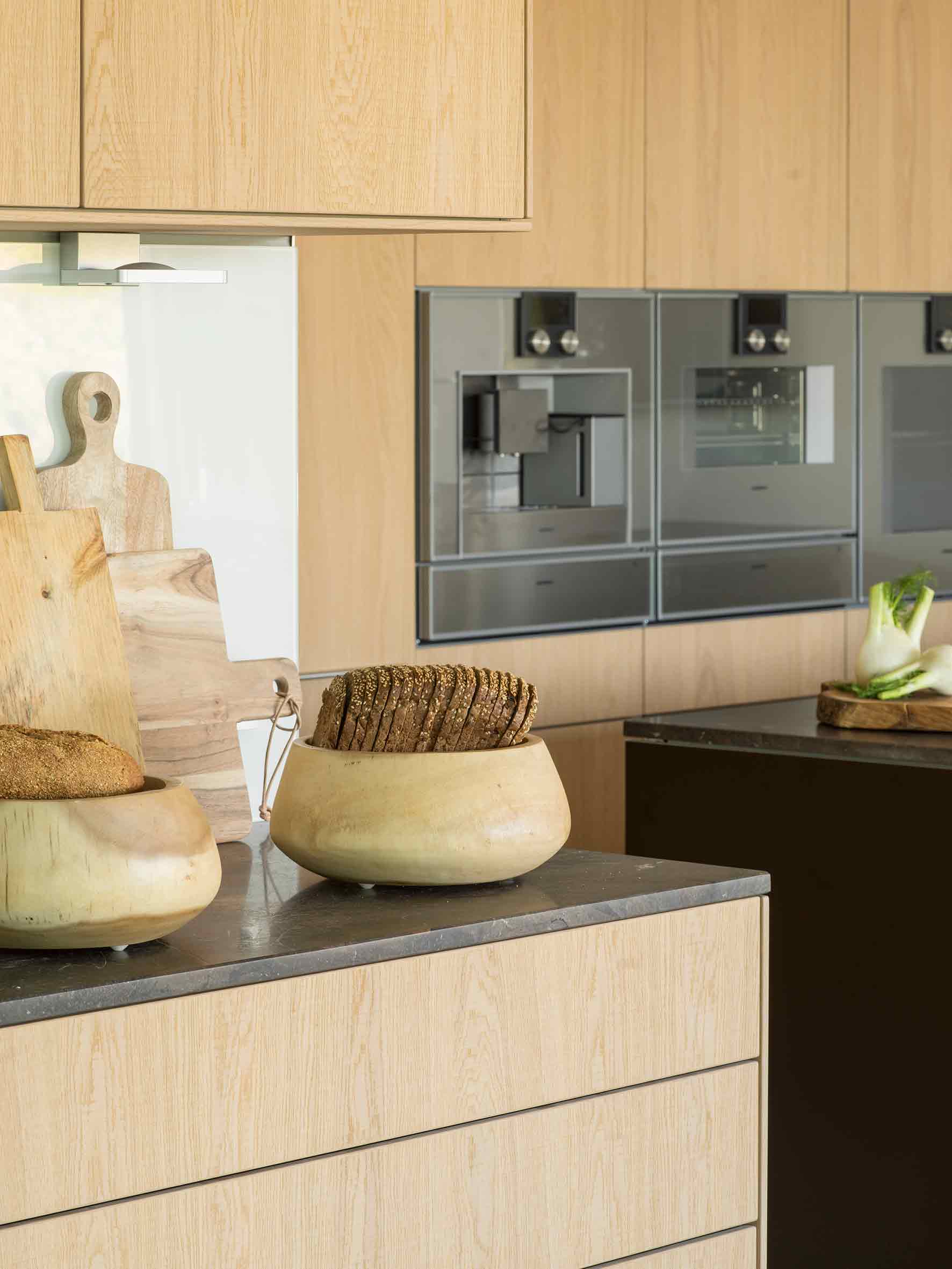 Detalle de encimera con cuencos de madera con pan, tablas de cortar y hornos empotrados