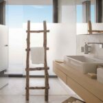 Baño con lavabo sobre mueble de roble, ducha de cristal translúcido y toallero de ramas rústicas