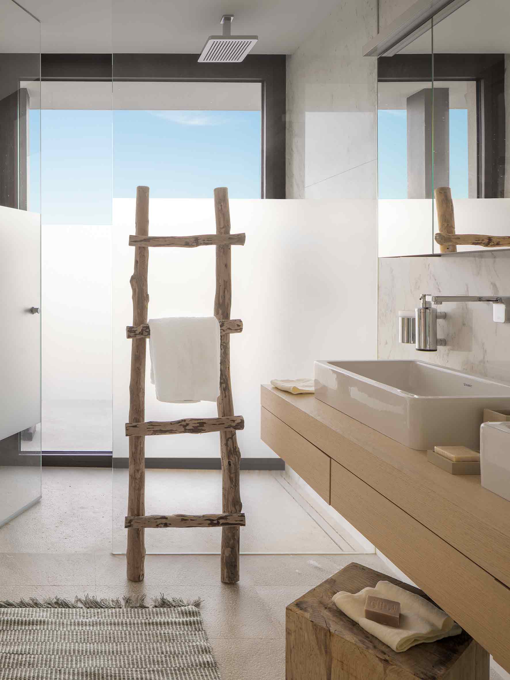 Baño con lavabo sobre mueble de roble, ducha de cristal translúcido y toallero de ramas rústicas