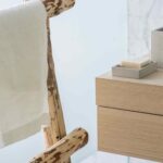 Detalle de toallero de ramas con toalla blanca, cajones de roble, jabón y pared de mármol