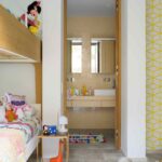 Dormitorio infantil con litera, peluches, papel pintado amarillo y puerta abierta a un baño beige