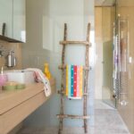 Baño infantil con toallero de ramas, toallas de colores, mueble de madera clara y alfombrilla con pompones