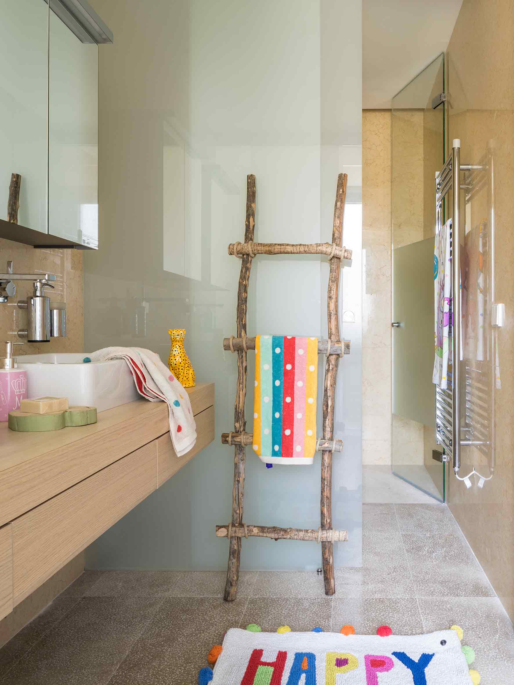 Baño infantil con toallero de ramas, toallas de colores, mueble de madera clara y alfombrilla con pompones