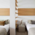 Dormitorio con dos camas separadas por un pilar blanco con baldas de madera y cabeceros de roble