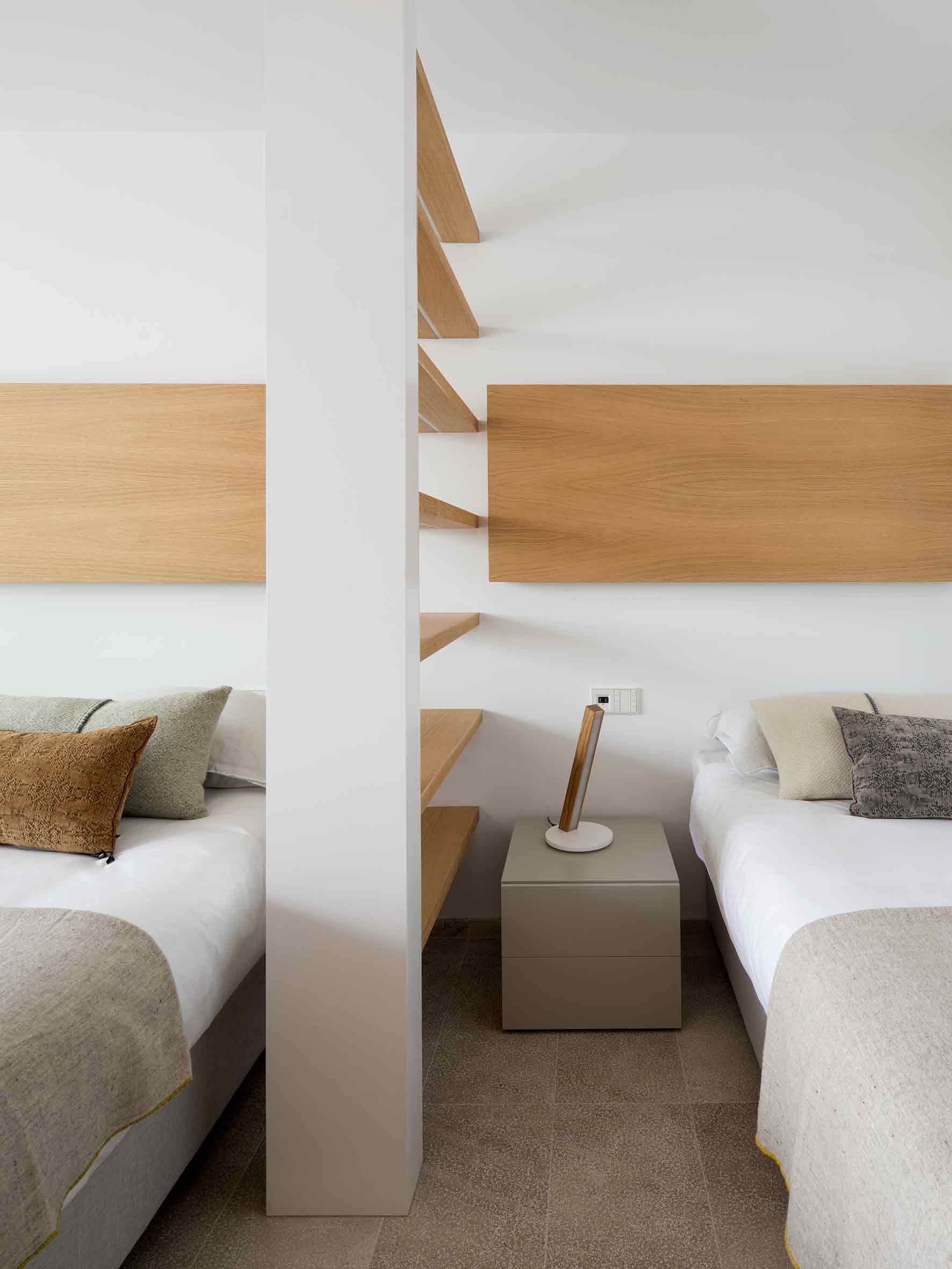 Dormitorio con dos camas separadas por un pilar blanco con baldas de madera y cabeceros de roble