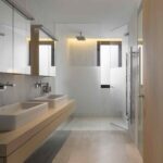 Baño con doble lavabo sobre encimera de roble, ducha de cristal y suelo de piedra clara
