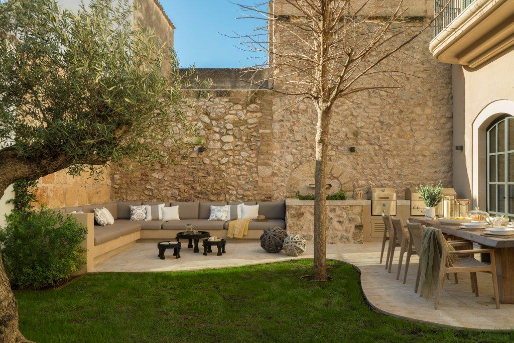 Jardín de Can Angel con sofá de obra, muro de piedra, olivo, césped y comedor exterior