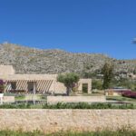 Muro bajo de piedra en primer plano, con la villa, una palmera y la montaña al fondo