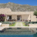 Fachada de piedra de la villa junto a la piscina, con tumbonas, olivo y montaña detrás
